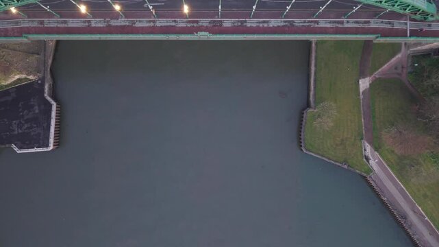 Top-down aerial drone shot flying over the Wearmouth Bridge in Sunderland at dawn, showcasing the green steel truss architecture and vehicles traveling across the river.