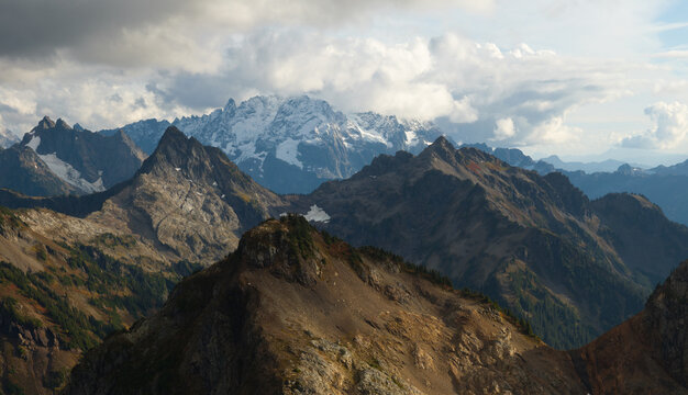 Aerial view of the rugged peaks and snow-capped summits of Winchester Mountain Lookout under a dramatic cloudy sky in Whatcom County, Washington, United States.