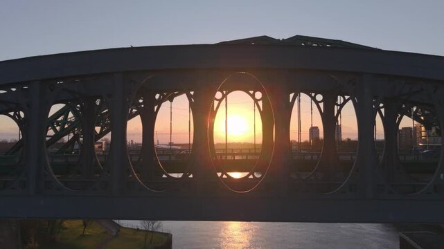 Aerial drone shot flying upwards and backwards from the silhouetted Wearmouth Bridge and Monkwearmouth Railway Bridge at sunrise, revealing the golden sun reflecting on the River Wear in Sunderland.