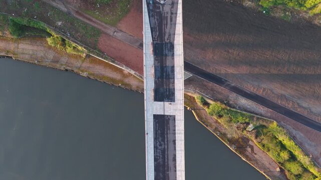 Top-down aerial drone tracking shot of a pedestrian walking across the Keel Crossing bridge in Sunderland at dawn, showcasing the modern architectural design and river landscape.