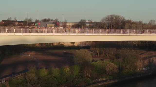 Aerial tracking shot flying sideways along the Keel Crossing pedestrian bridge in Sunderland at sunrise, showing the modern architecture and urban landscape.
