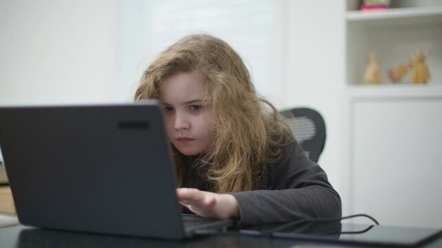 School kid study online. Child typing on laptop at home. Child focused on laptop screen. Child learning online education. Child studying schoolwork on laptop.