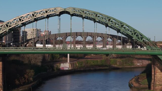 Aerial telephoto shot tracking slowly toward the Wearmouth Bridge and Monkwearmouth Railway Bridge in Sunderland during the morning commute, highlighting the historic industrial architecture.
