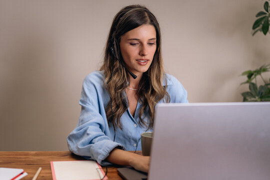 Female customer support agent working remotely with headset and laptop at home. A dynamic professional woman with a headset multitasking between online meetings and remote work on a laptop.