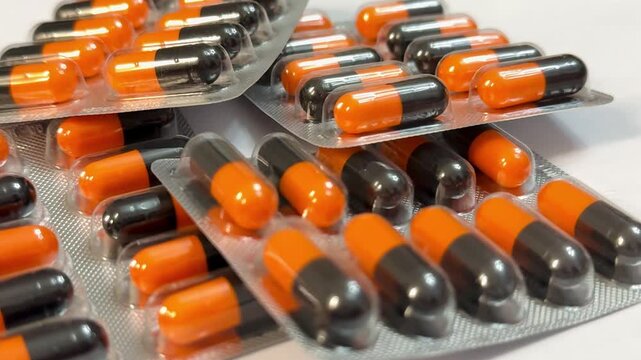 Orange And Black Capsules In Blister Pack, Closeup Showing Glossy Capsules Arranged In Foil Trays, Pharmacy Storage And Packaging Scene With Emphasis On Dosage, Sterile Clinical Lighting.