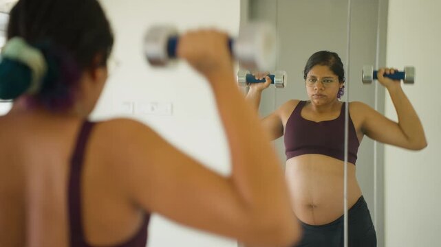 Indian female third trimester of pregnancy gym mirror reflection does dumbbell press exercises