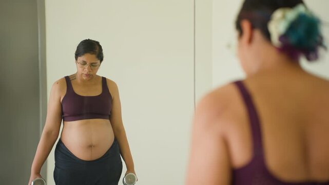 Indian female third trimester of pregnancy gym mirror reflection does dumbbell bicep curls exercises