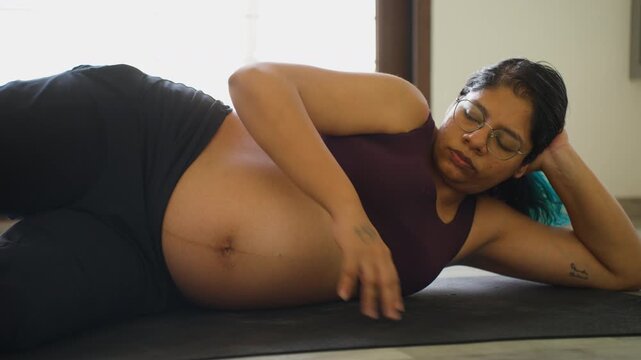 Pregnant Indian female close up doing stretching leg exercises on yoga mat during third trimester