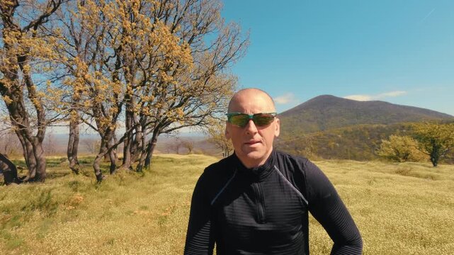Active mature man in his 50s running on a trail through a scenic field and forest on a sunny spring day. Healthy senior lifestyle, jogging and exercising outdoors. High quality 4k footage.