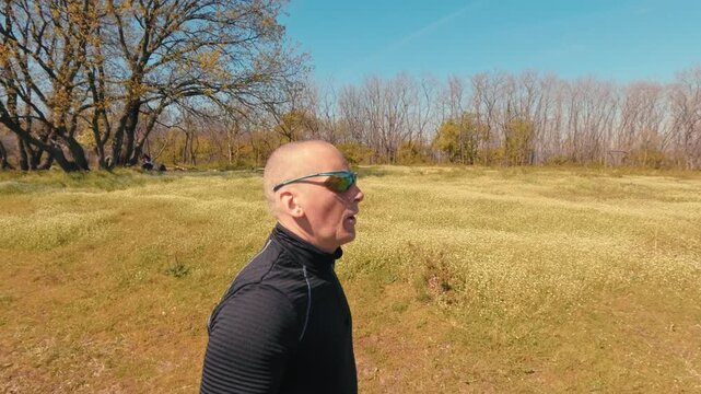 Close up shot of a mature man in his 50s running in nature. Focus on his face, sunglasses, and emotions during an active outdoor jogging session on a sunny day.