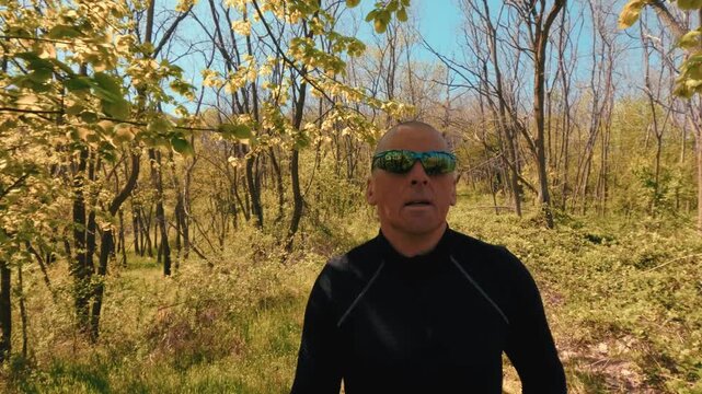 Vertical portrait orientation of a mature man jogging in nature. Seamless footage for mobile screens, Reels, and TikTok stories. Active lifestyle of seniors in their 50s.