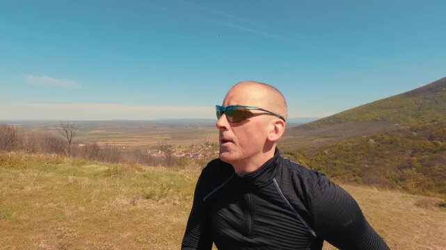Close up shot of a mature man in his 50s running in nature. Focus on his face, sunglasses, and emotions during an active outdoor jogging session on a sunny day.