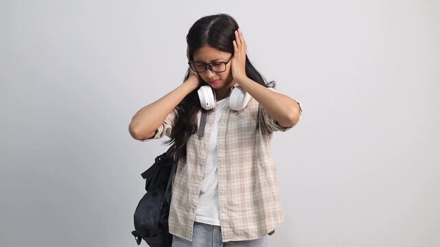 Unhappy sad angry young asian female college student close eyes and cover ears by hands being annoyed with loud noise, isolated white studio background, emotions, dislike loud sounds