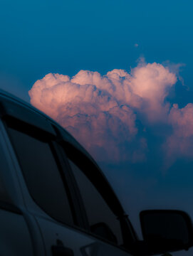 Select focus. A beautiful fluffy Dramatic sunset cloud formation at golden hour, framed by a car silhouette.