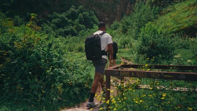 Hikers walk through a lush valley and pass a sign reading &ldquo;Have a nice trip,&rdquo; capturing travel spirit, positivity, and scenic outdoor adventure.