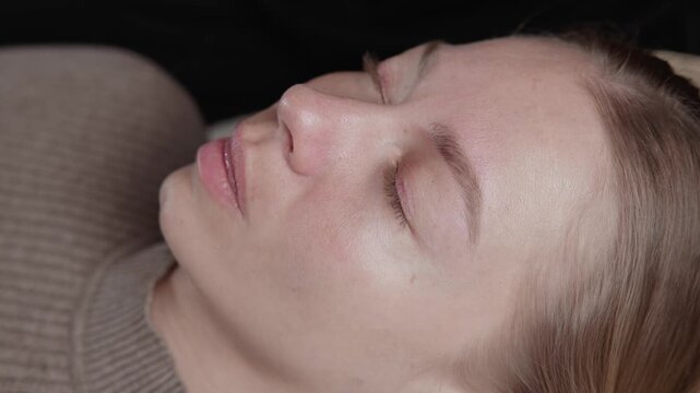 Female after permanent eyeliner tattoo application on closed eyelid in beauty salon.