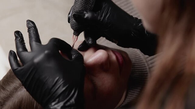 Macro tracking shot of eyeliner tattooing on client's face in studio with gloved hand moving needle in slow motion.