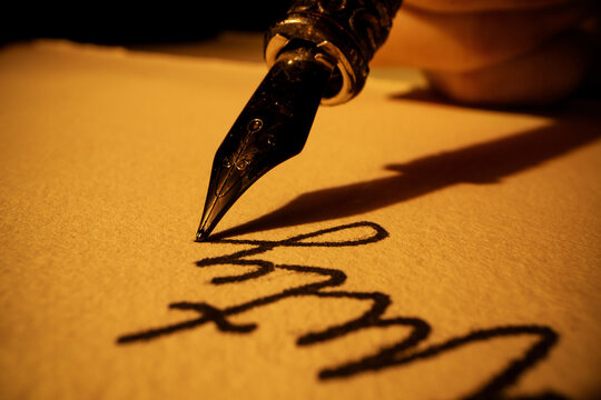 closeup of hand writing letter with vintage quill pen and ink on old parchment paper