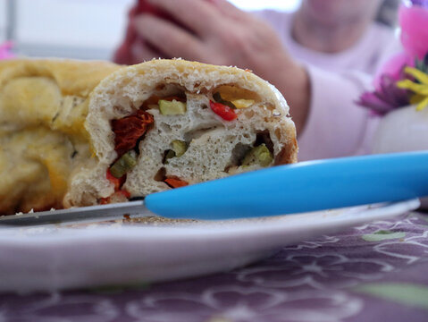 Dettaglio di una fetta di torta salata rustica farcita con verdure e pomodori, servita su un piatto bianco durante un pranzo festivo di Pasqua in famiglia