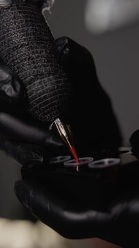 Closeup of tattoo machine to pigment of paint red ink into ink caps in tattoo studio.