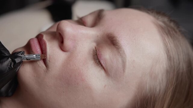 Portrait of woman applying permanent tattoo makeup on lips in beauty salon, Procedure microblading.