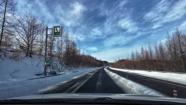 Point of view driving on a long curved highway after crossing a bridge in a snowy mountain landscape. Clean empty road with no traffic, cinematic winter driving scene