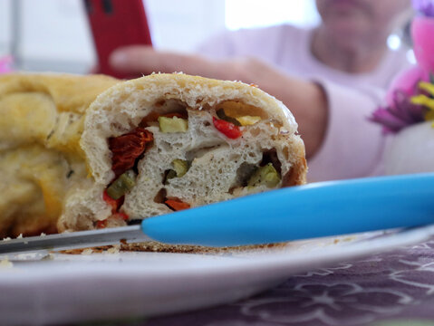 Dettaglio di una fetta di torta salata rustica farcita con verdure e pomodori, servita su un piatto bianco durante un pranzo festivo di Pasqua in famiglia