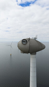 Aerial view of the Westermeerdijk wind turbine nacelle with its unique oval shape and viewing window over the calm waters of the IJsselmeer under a cloudy sky in Espel, Flevoland, Netherlands.