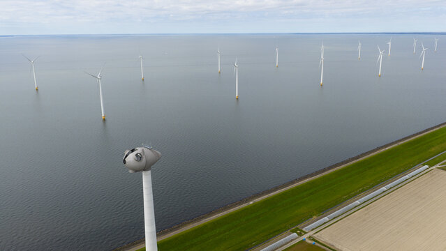 Aerial view of the Westermeerdijk wind farm with turbines standing in the water along the green dike and agricultural fields in Espel, Flevoland, Netherlands.