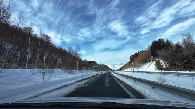 Point of view driving on a winter highway where the road widens from two lanes to four lanes along a curved snowy landscape. Clean empty road with no traffic