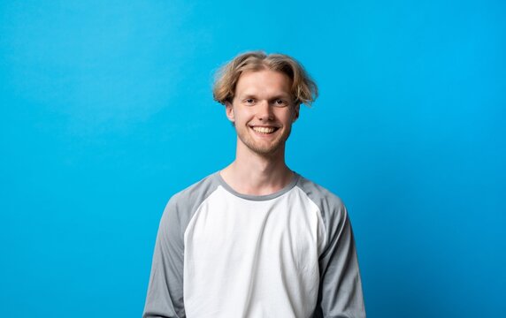 Young blonde man with a happy smile posing against a blue background, portraying confidence, youthfulness, and positive emotions, ideal for concepts of well-being and contentment
