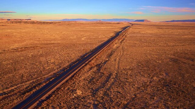 Drone aerial of heavy freight train crossing arid western terrain, transportation system, supply chain, logistics