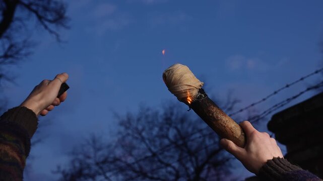 A person hands light a homemade torch with a lighter outdoors in the evening. Concept of survival, preparation, outdoor activity, camping, and primitive fire making for lifestyle and advertising use.