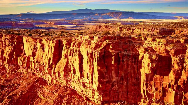Drone shot of New Mexican Landscape flying away from red rock mesa revealing the rock face bathed in sunset colors