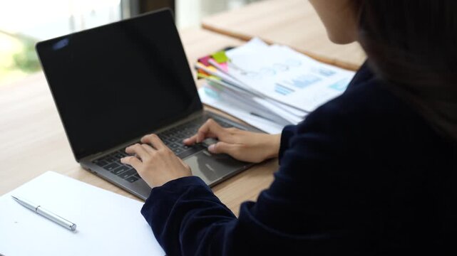 Businesswoman hands typing on a laptop keyboard while working on a project in the office, analyzing financial documents, graphs, and market data for strategic planning