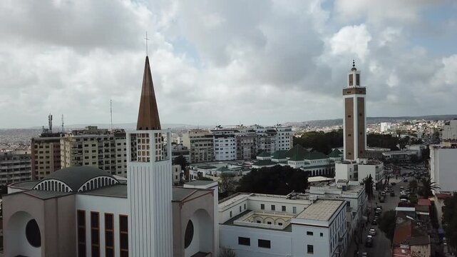 Cinematic drone shot of a mosque minaret and church spire standing together in Tangier, Morocco, symbolizing religious tolerance and coexistence.