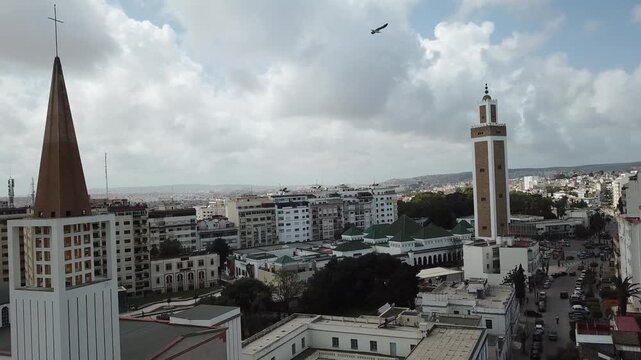 Cinematic drone shot of a mosque minaret and a church spire stand side by side in Tangier, Morocco, representing a long history of religious tolerance.