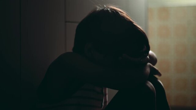 Close view of child hiding face in arms while sitting on floor expressing intense emotional pain depression and trauma with sense of isolation and vulnerability