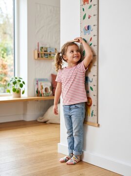 A child measuring their height against the wall at home, happy with their growth and development.