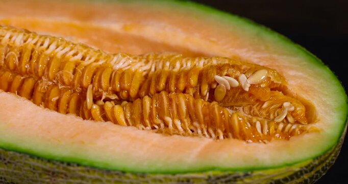The melon was cut in the studio, a ripe orange melon with numerous beige seeds in a juicy pulp under even light with clear details and organic texture in the macro.