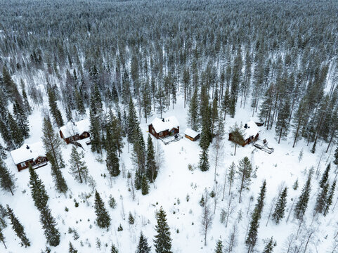 Aerial view of wooden cabins nestled among snow-covered pine trees in a vast winter forest Lapland, Finland.