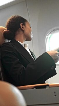 Passenger in business attire sits by an airplane window, reading a document in a modern cabin with tan leather seats.