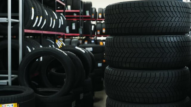 Stack of black rubber tires displayed in a tire shop with shelves filled with additional tires in the background, showcasing various tread patterns and sizes