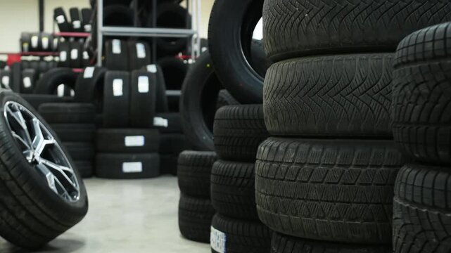 Stack of black rubber tires displayed in a tire shop with shelves filled with additional tires in the background, showcasing various tread patterns and sizes