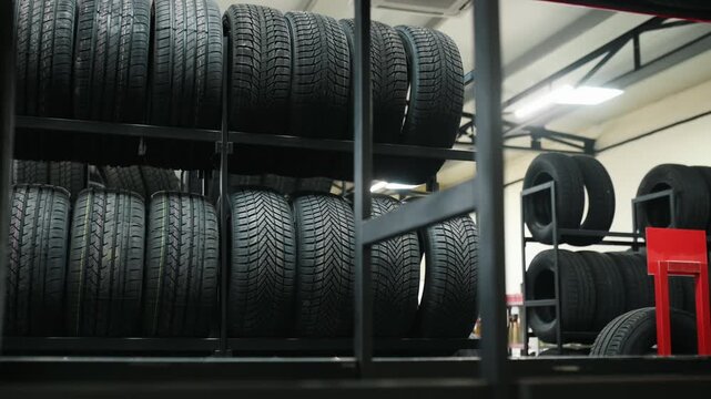 Close-up of four black car tires with visible tread patterns, arranged in a stacked formation inside a well-lit automotive workshop