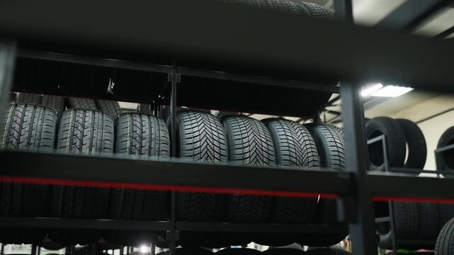 Stack of black rubber tires arranged neatly on metal shelving inside a tire storage facility with industrial lighting and a clean, organized layout