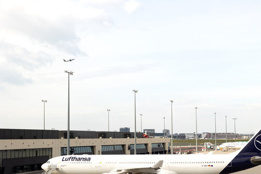 Airport Frankfurt am Main, Germany, April 11, 2026. - Flying Lufthansa airplane on the sky and another on the the airfield of Terminal 3. Handling area for passenger aircraft. Blue sky with clouds. 