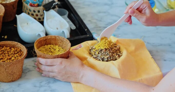 Woman hands pouring dried botanicals into cloth pouch, indoor hotel wellness workshop, spa resort activities for guests, handmade aromatherapy products marketing
