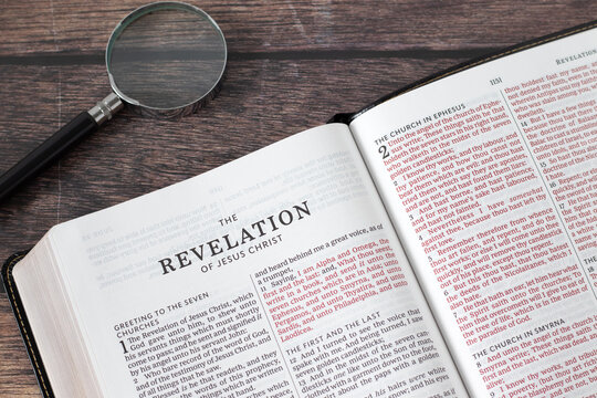 Holy bible book of revelation with magnifying glass on wooden table. Top view. Christian prophecy study, biblical concept.