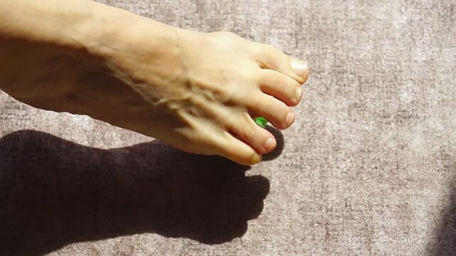 Top view of foot rolling textured massage ball forward and backward in steady linear motion in sunlight. Captures repetitive movement pattern, rhythmic stimulation, and simple home wellness practice.